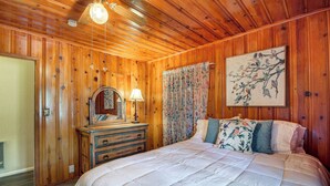 Een slaapkamer met houten lambrisering, een bed, een kast en kunstwerken.