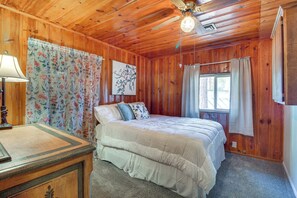 Une chambre à coucher aux murs lambrissés, avec un lit, une table de chevet, une lampe et une fenêtre avec des rideaux.