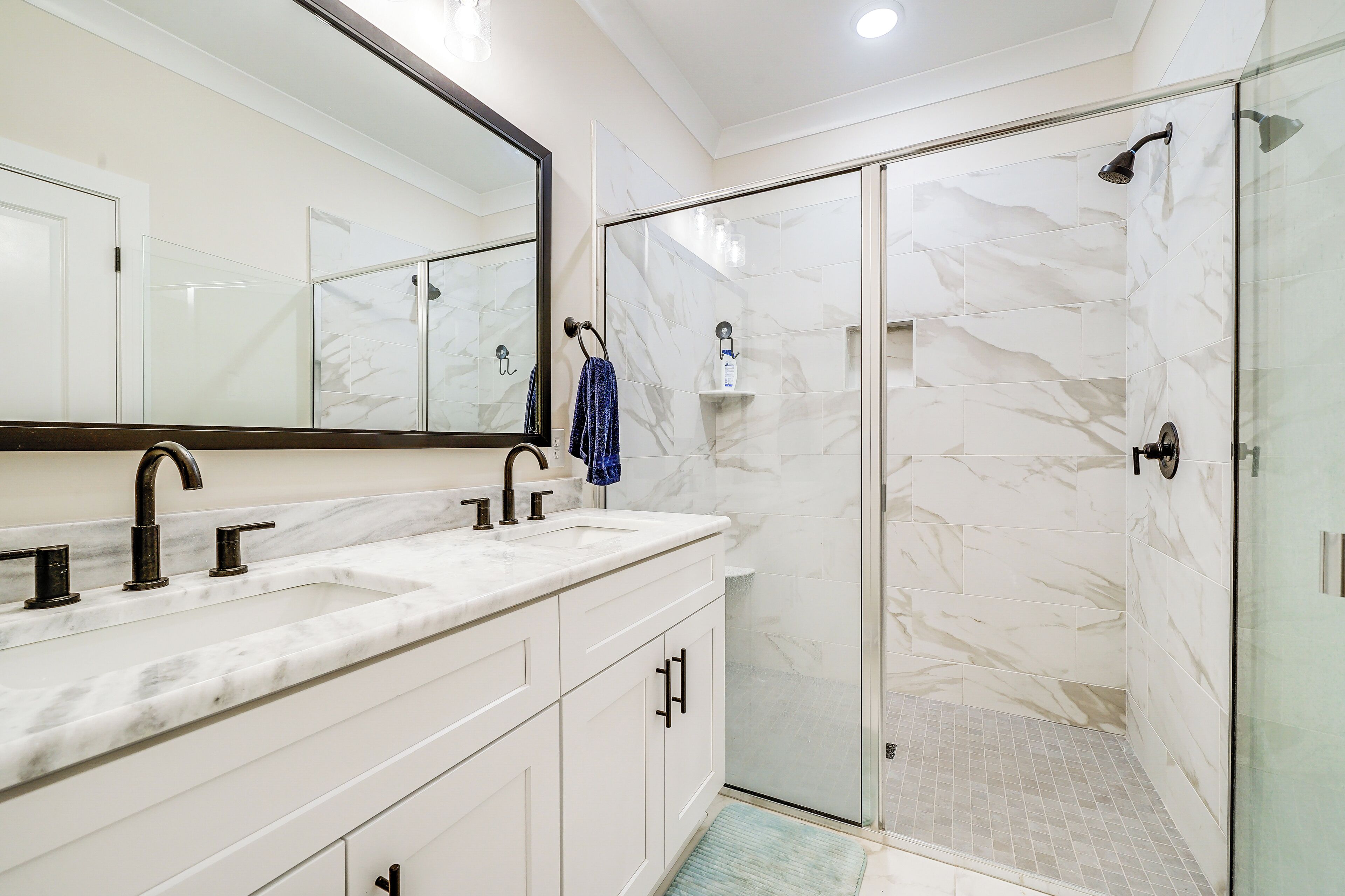 A modern bathroom with a large mirror, a marble countertop, and a glass-enclosed shower.