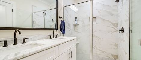 A modern bathroom with a large mirror, a marble countertop, and a glass-enclosed shower.