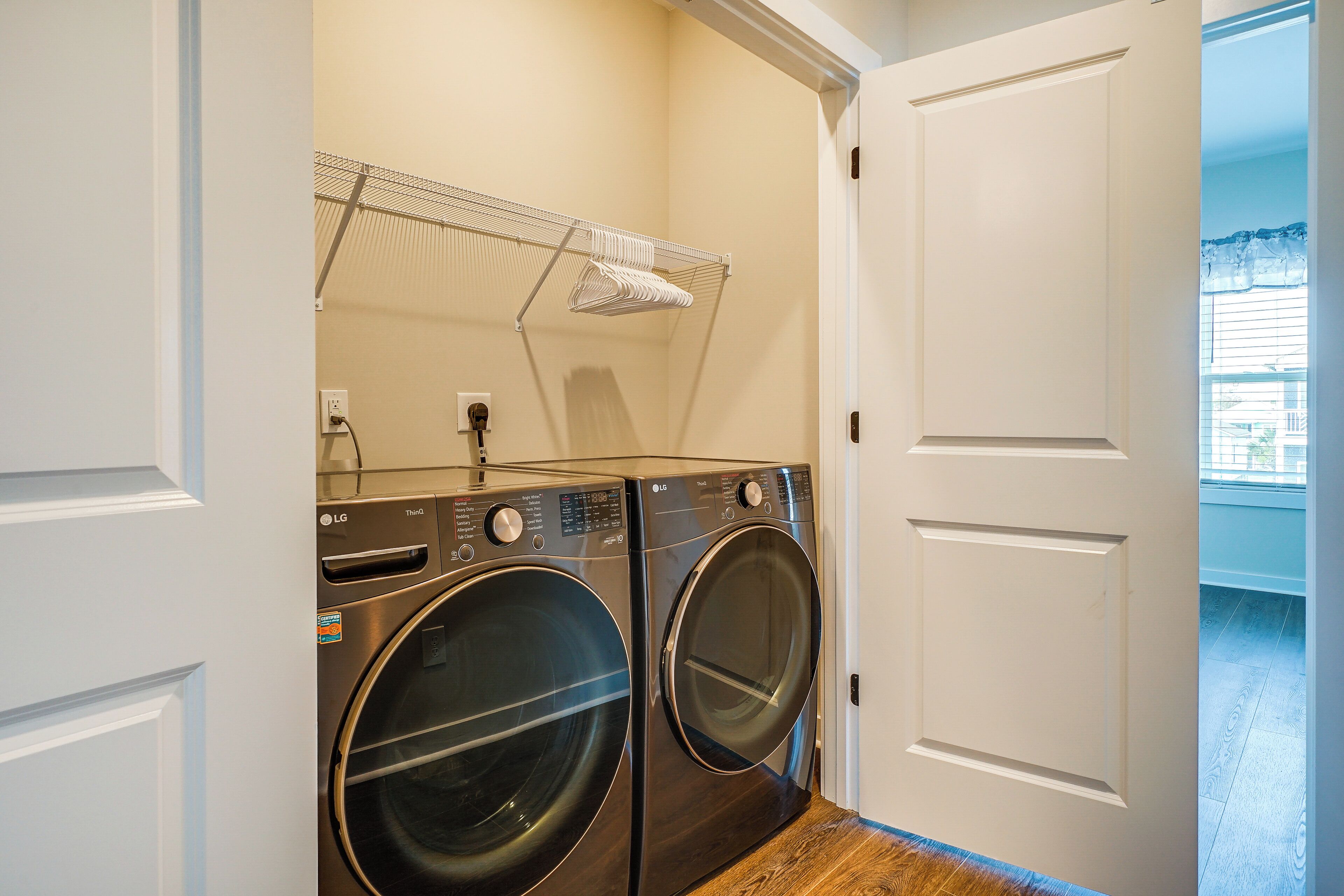 A laundry room with two front-loading LG washers and dryers, a metal drying rack, and a door leading to a balcony.