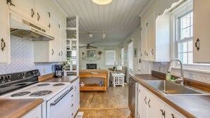 A kitchen with white cabinets, a stove, and a sink. There is a wooden bench and a small table with a lamp. - Carolina Beach Home w/ Private Deck: Walk to Shore (Carolina Beach)