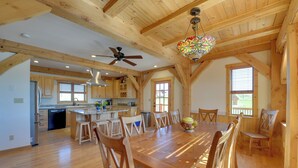 Une cuisine spacieuse avec des poutres apparentes, un coin repas doté d’une grande table en bois et un ventilateur de plafond.