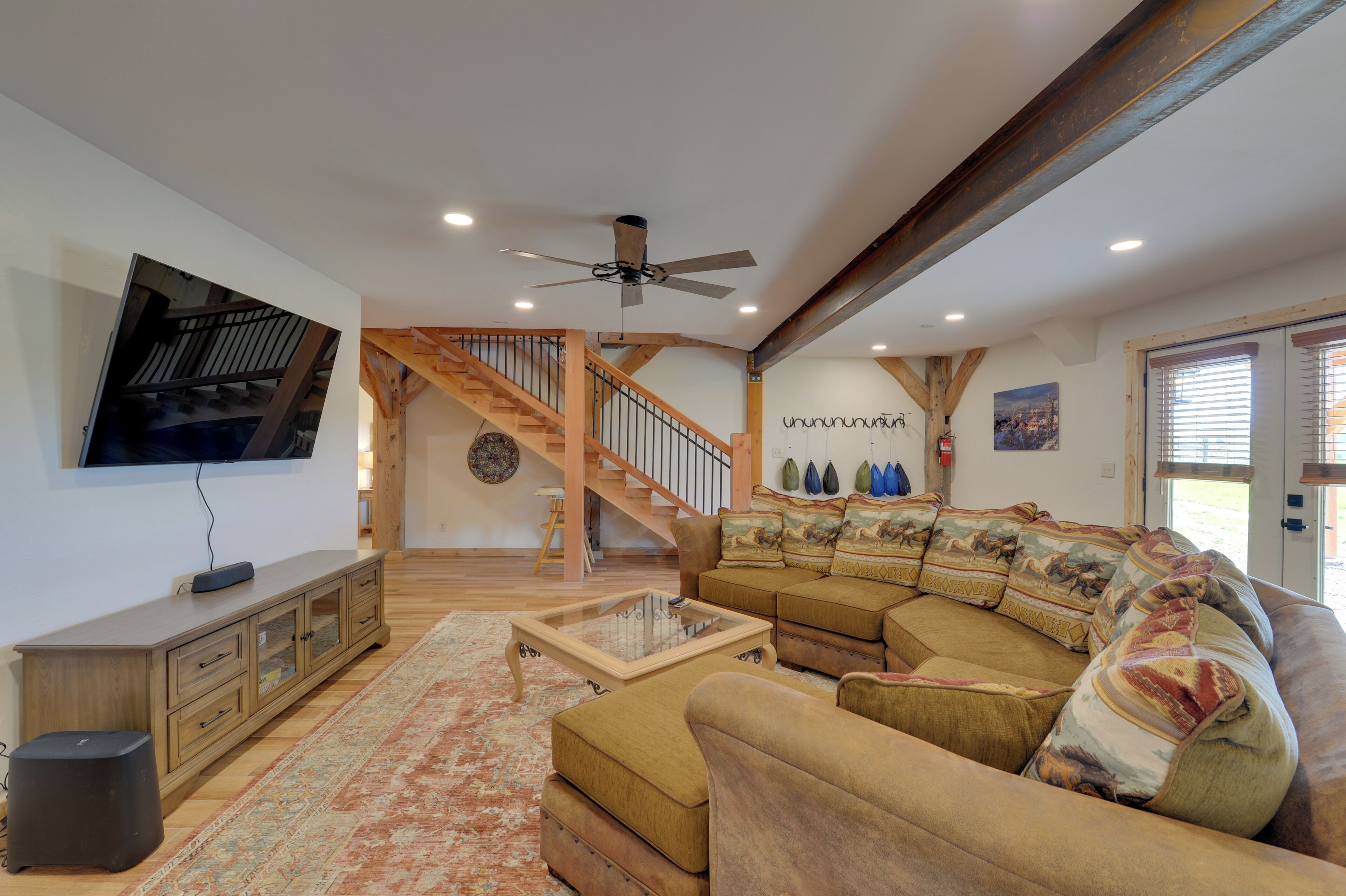 A spacious living room with a large sectional sofa, a glass coffee table, and a wooden staircase.