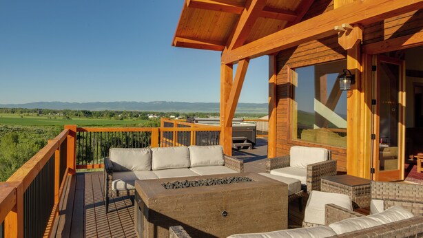Une terrasse en bois avec des sièges extérieurs, un foyer et une vue sur la campagne.