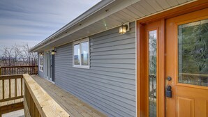 A wooden deck with a railing, a gray exterior wall, and a wooden door with a glass panel.