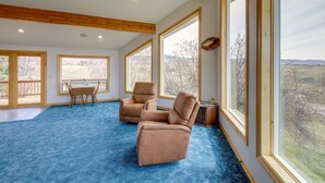 A spacious room with large windows, a blue carpet, and two leather chairs.