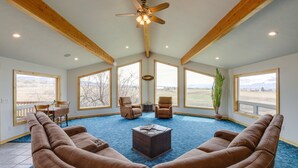 A spacious living room with a large sectional sofa, two recliners, a coffee table, and a ceiling fan. Large windows offer views of the outdoors.