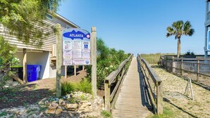 Un muelle de madera que conduce a una zona de playa, con un cartel que muestra normas e información.