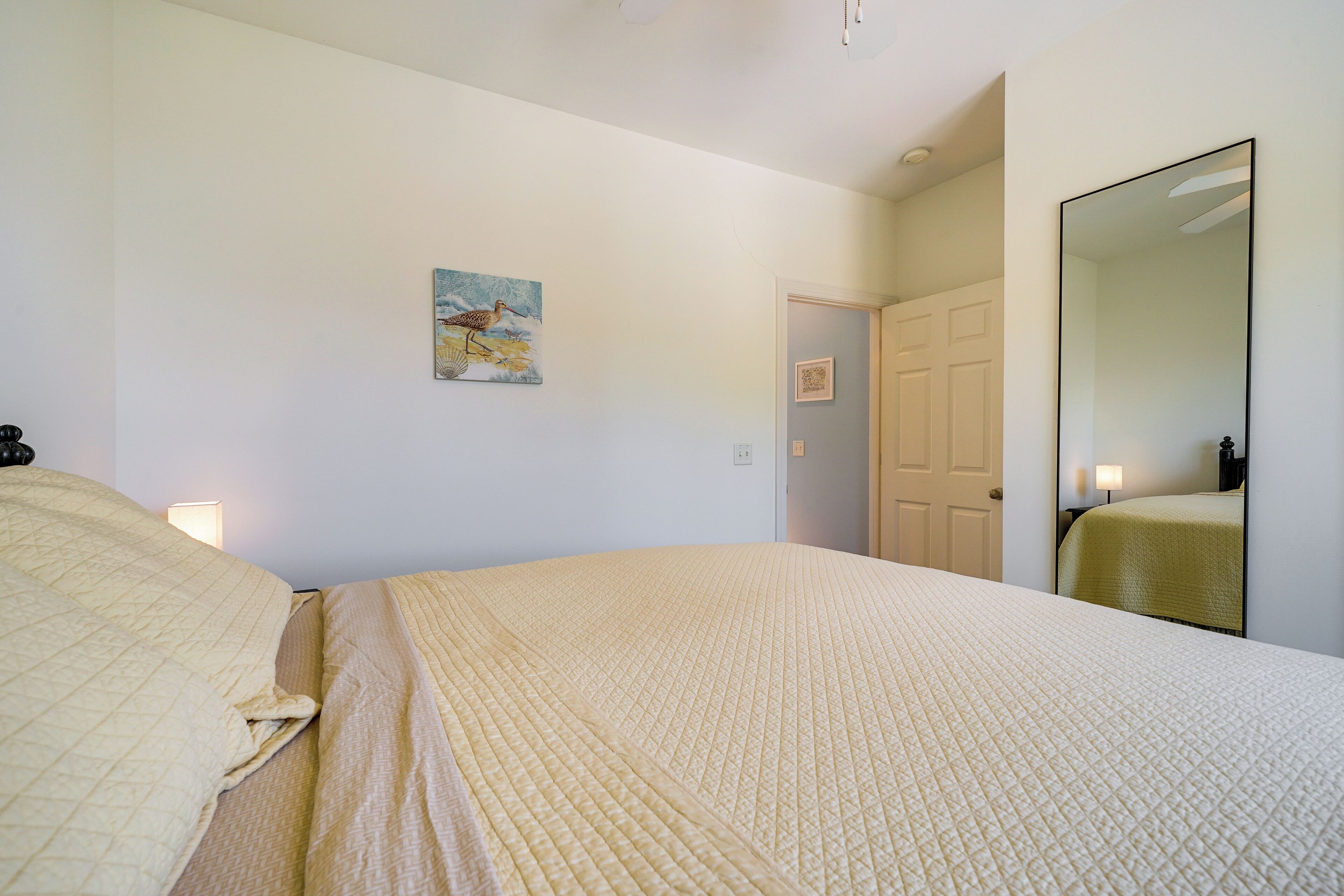 A bedroom with a bed, a painting, a door, and a mirror.