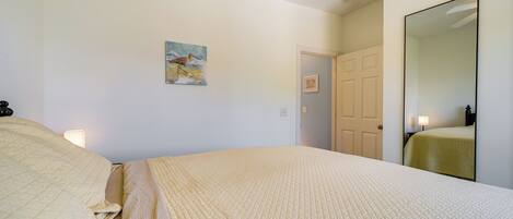 A bedroom with a bed, a painting, a door, and a mirror.
