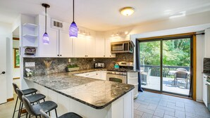 A modern kitchen with a large island, bar stools, white cabinets, and a sliding glass door to a deck. - Lakefront New York Abode w/ Deck, Grill & Fire Pit (Mahopac)