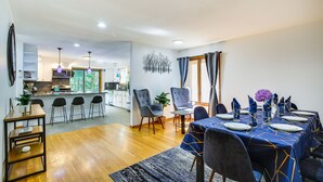 A modern dining area with a blue tablecloth, wooden chairs, and a kitchen in the background. - Lakefront New York Abode w/ Deck, Grill & Fire Pit (Mahopac)