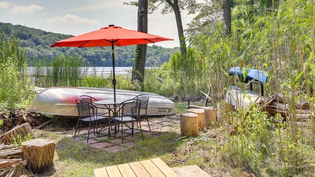 A lakeside outdoor seating area with a red umbrella, metal chairs, and a canoe. - Lakefront New York Abode w/ Deck, Grill & Fire Pit (Mahopac)