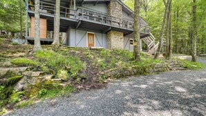 Une cabane moderne avec des fondations en pierre, une porte d’entrée en bois et un balcon donnant sur une zone boisée.