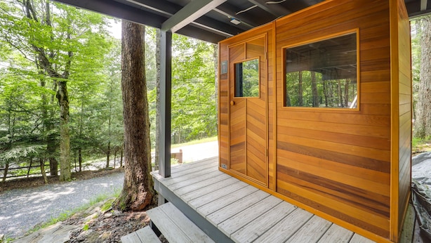 Une cabane en bois dotée d’une grande fenêtre et d’une porte, entourée d’arbres.
