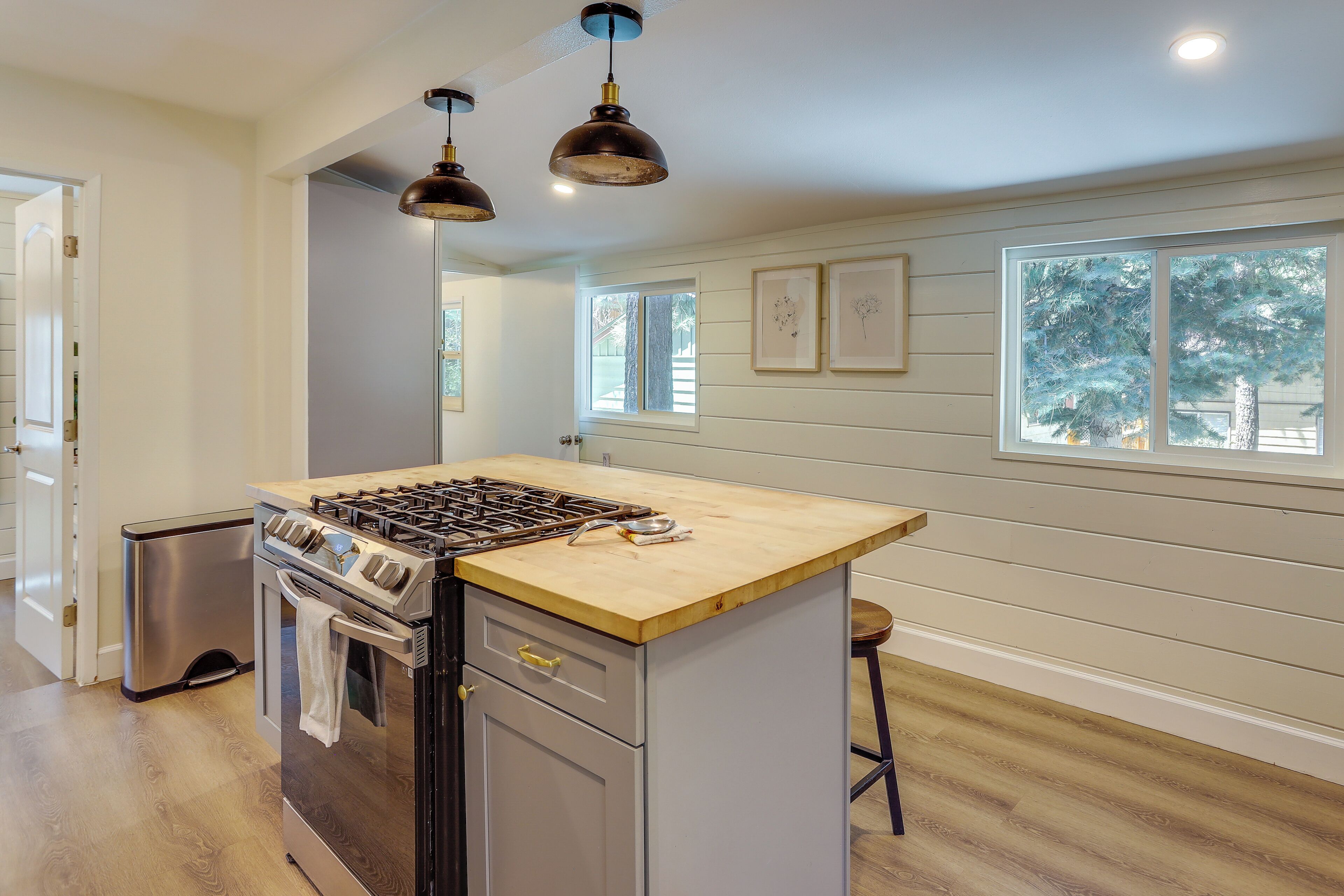 A kitchen with a central island, stainless steel appliances, pendant lighting, and large windows.