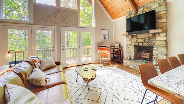 A spacious living room with a stone fireplace, leather sofa, and a dining area. - Wooded Retreat w/ Decks & Views in Beech Mountain! (Banner Elk)