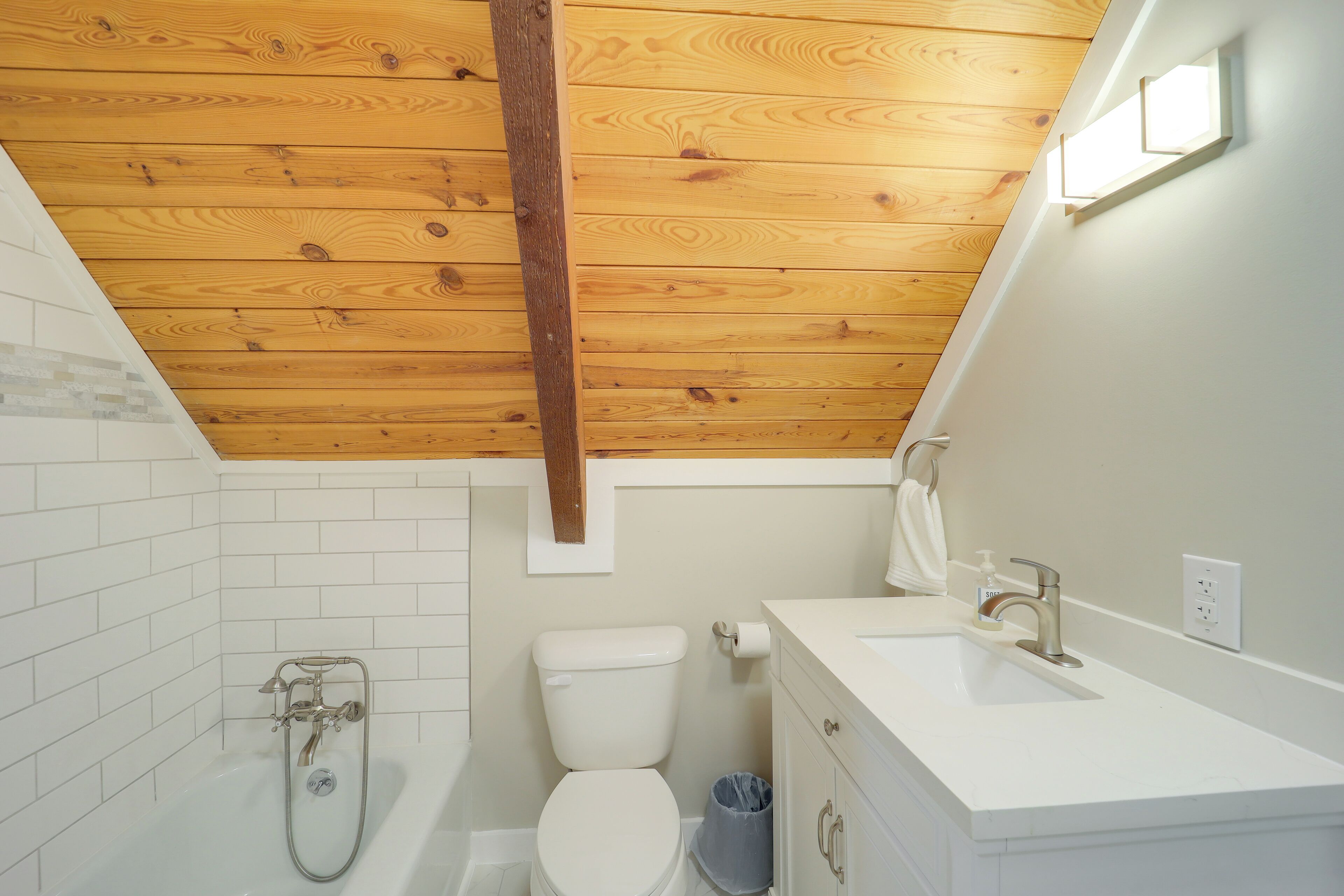 Een moderne badkamer met een houten plafond, witte tegels, een bad, een toilet en een wastafel.
