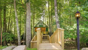 A wooden cabin with a green roof, surrounded by tall trees and a wooden staircase leading to it. - Wooded Retreat w/ Decks & Views in Beech Mountain! (Banner Elk)