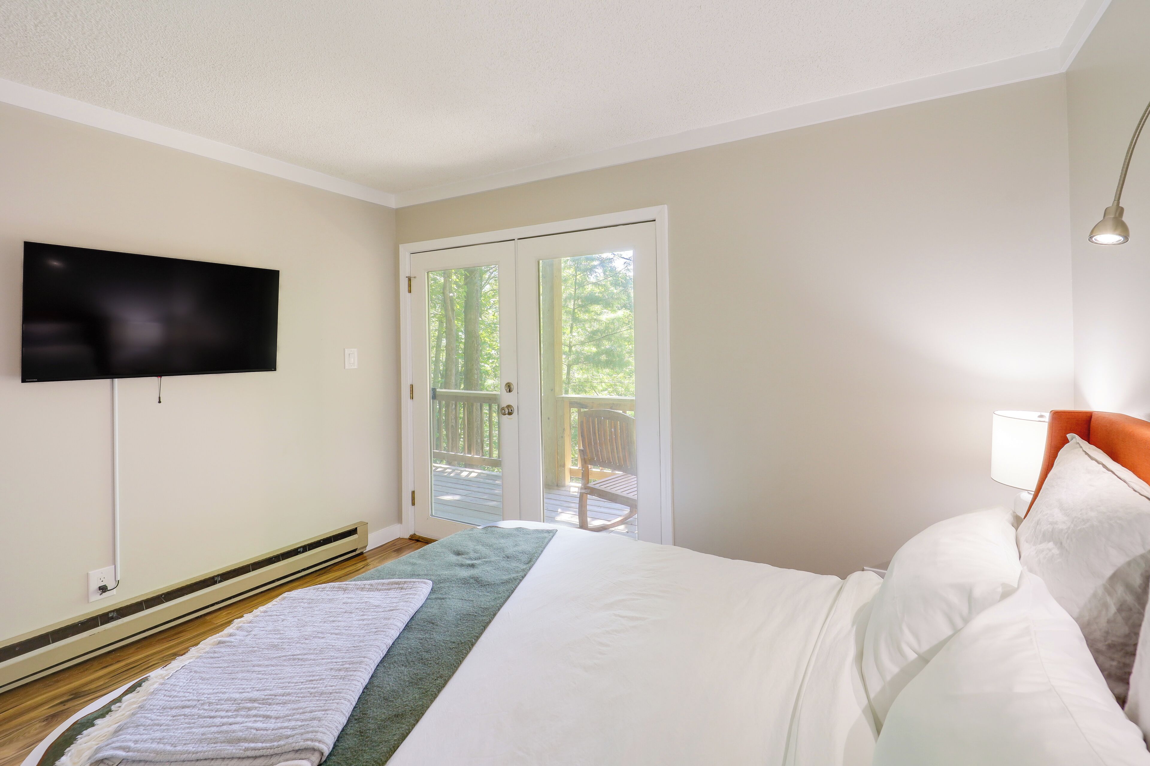 Un dormitorio con una cama, un televisor de pantalla plana montado en la pared, una puerta corrediza de vidrio que da a una terraza exterior y una mesita de noche con lámpara.