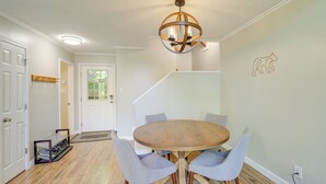 A dining area with a round wooden table, four grey chairs, a chandelier, and a staircase in the background. - Wooded Retreat w/ Decks & Views in Beech Mountain! (Banner Elk)