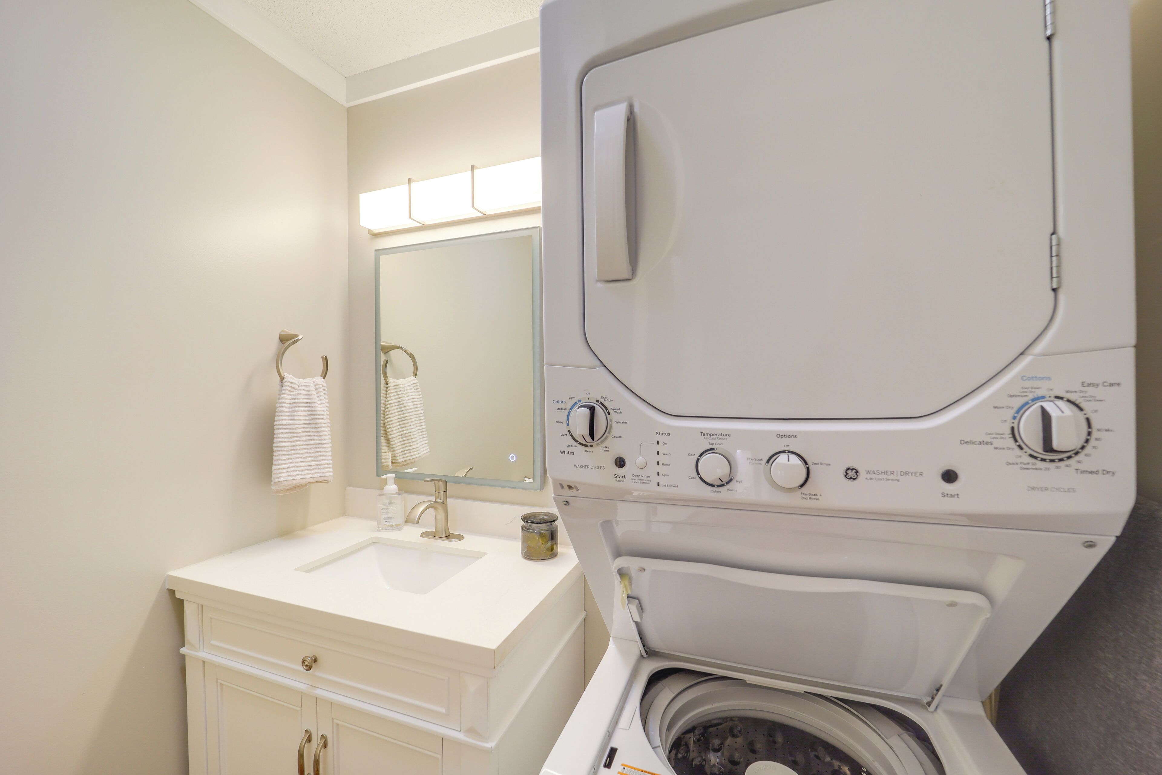 Un baño moderno con un lavamanos blanco, un espejo y una lavadora de carga frontal.