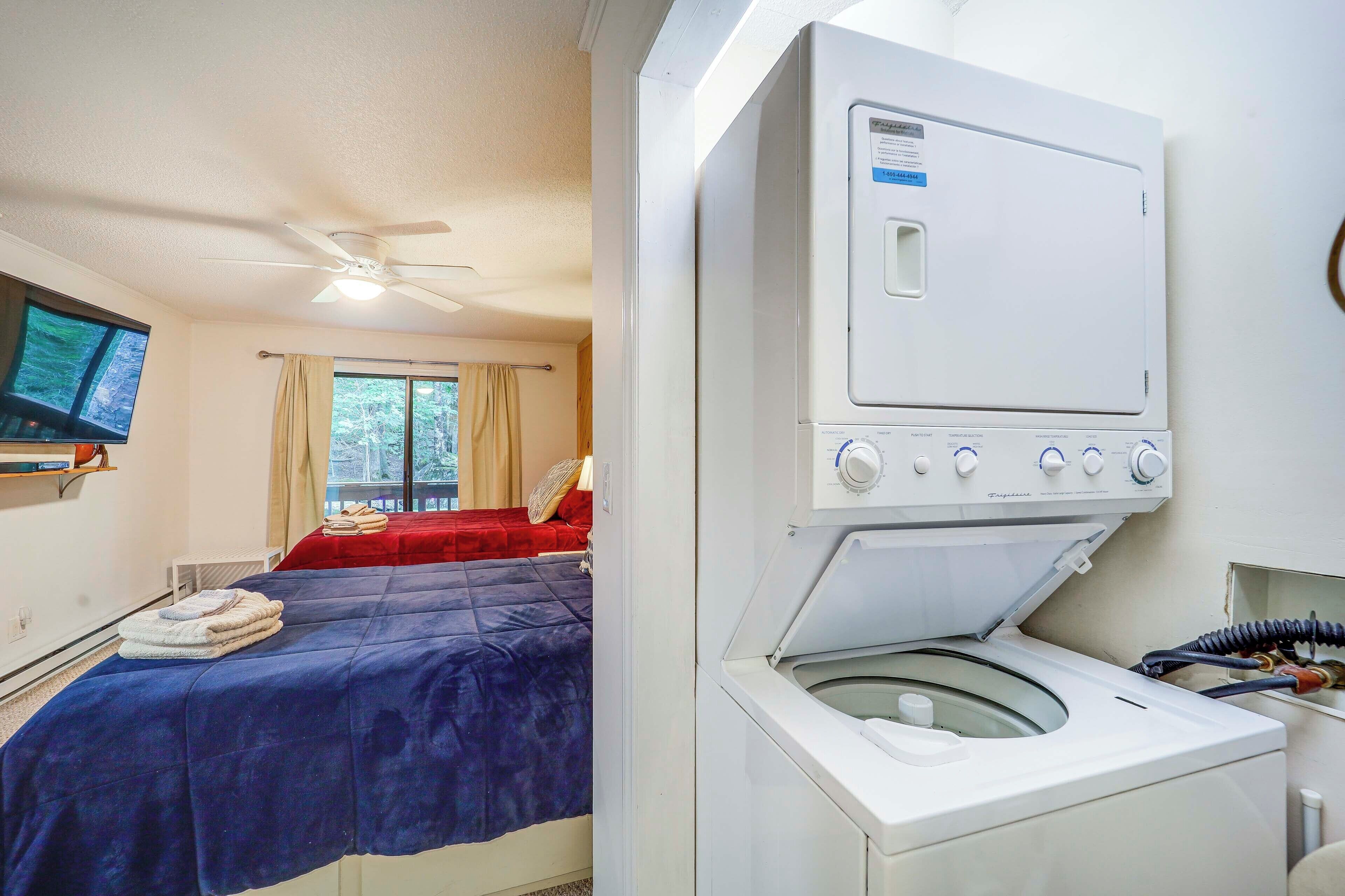 A hotel room with a bed, a ceiling fan, a washing machine, and a television on the wall.