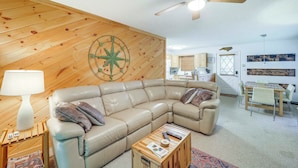 A cozy living room with a sectional sofa, a wooden accent wall, a ceiling fan, and a dining area. - Ski, Hike & Explore! All-season Condo in Beech Mtn (Banner Elk)