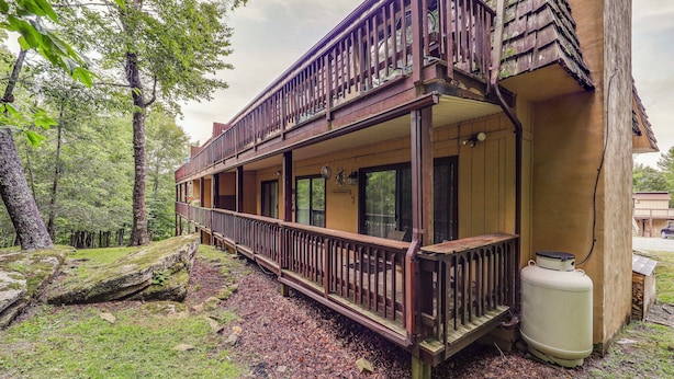 A wooden cabin with a balcony, surrounded by trees and a large moss-covered rock. - Ski, Hike & Explore! All-season Condo in Beech Mtn (Banner Elk)