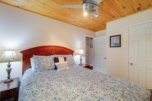 A bedroom with a wooden ceiling, a bed with patterned bedding, two bedside lamps, and a door. - All-season Retreat w/ Deck in Beech Mountain! (Banner Elk)