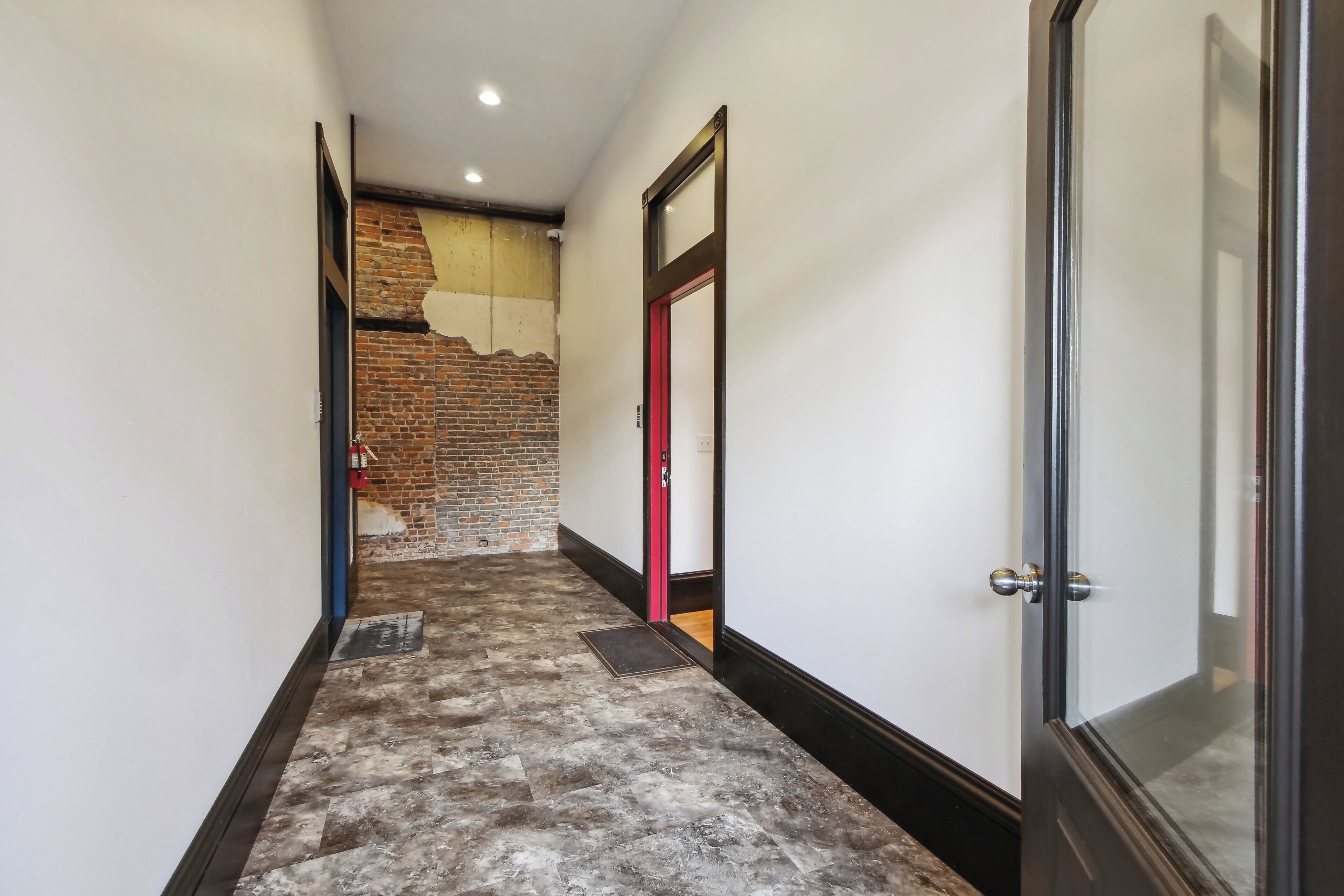 A hallway with a brick wall, a red door, and a glass door.