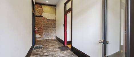 A hallway with a brick wall, a red door, and a glass door.