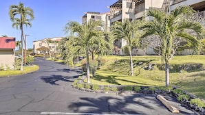 A residential street with modern buildings, palm trees, and a clear sky.