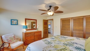 A bedroom with a bed, wooden wardrobe, a chair, a dresser, a ceiling fan, and a mirror.