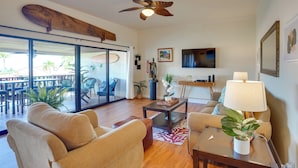 A spacious living area with a ceiling fan, a surfboard, a large window, and a dining area visible through glass doors.