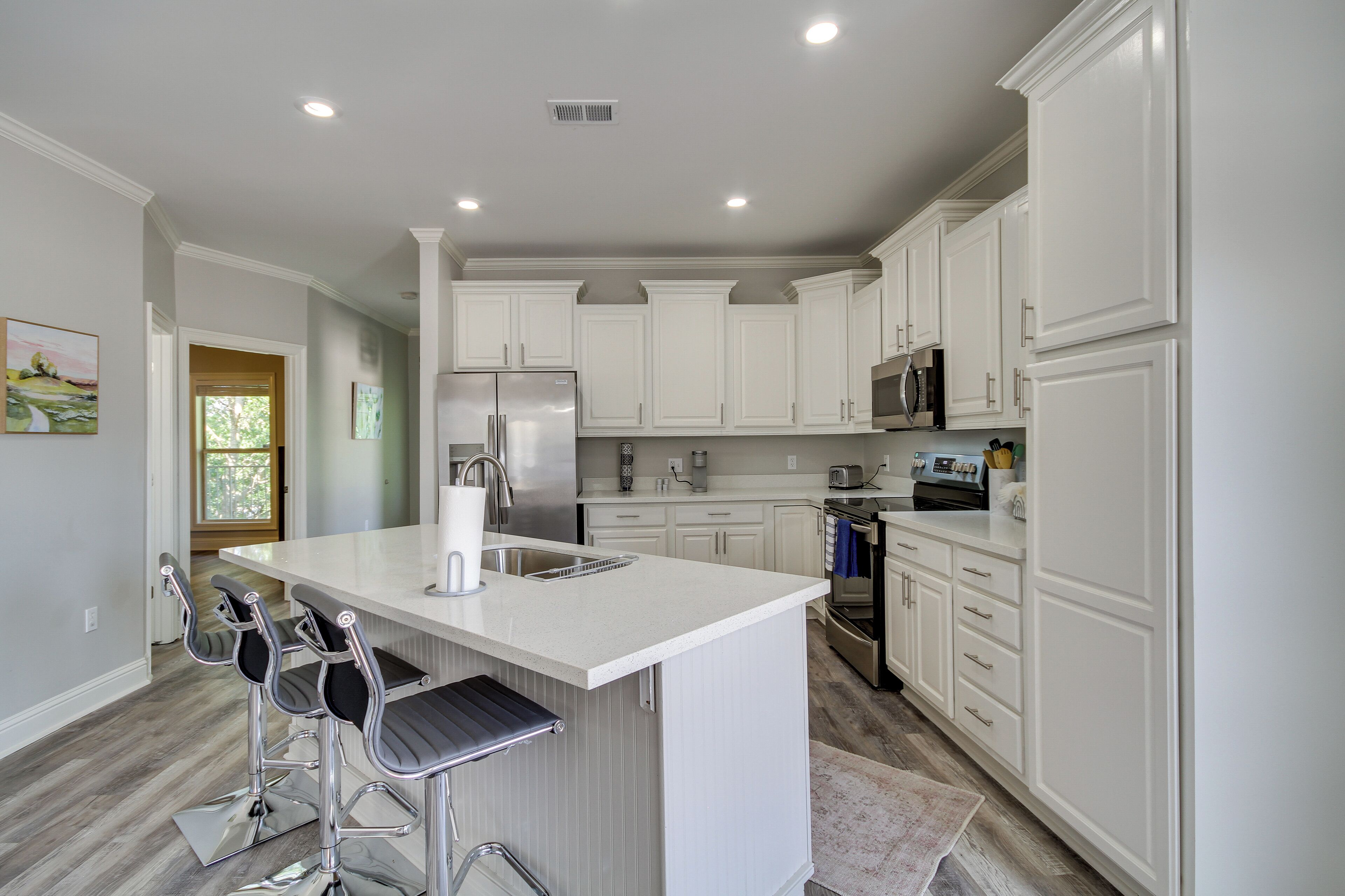 A modern kitchen with white cabinetry, stainless steel appliances, and a central island with bar stools.