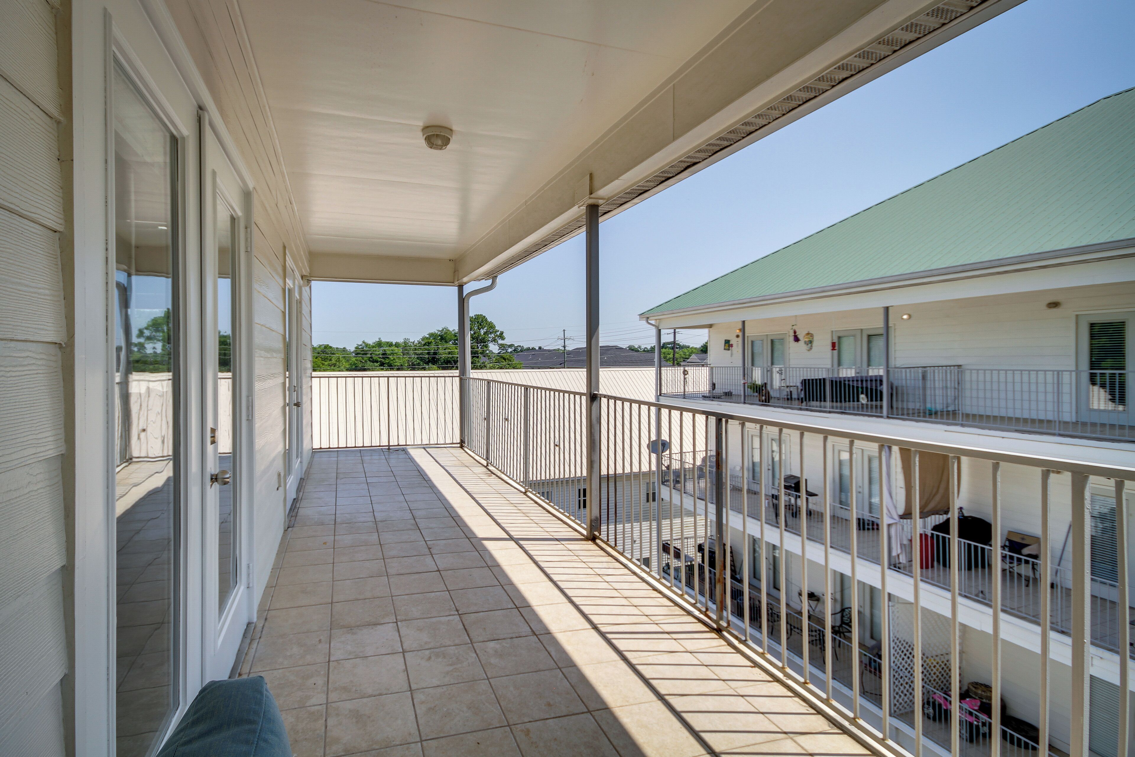 A covered balcony with a tiled floor, metal railing, and a view of a building with multiple windows and balconies.