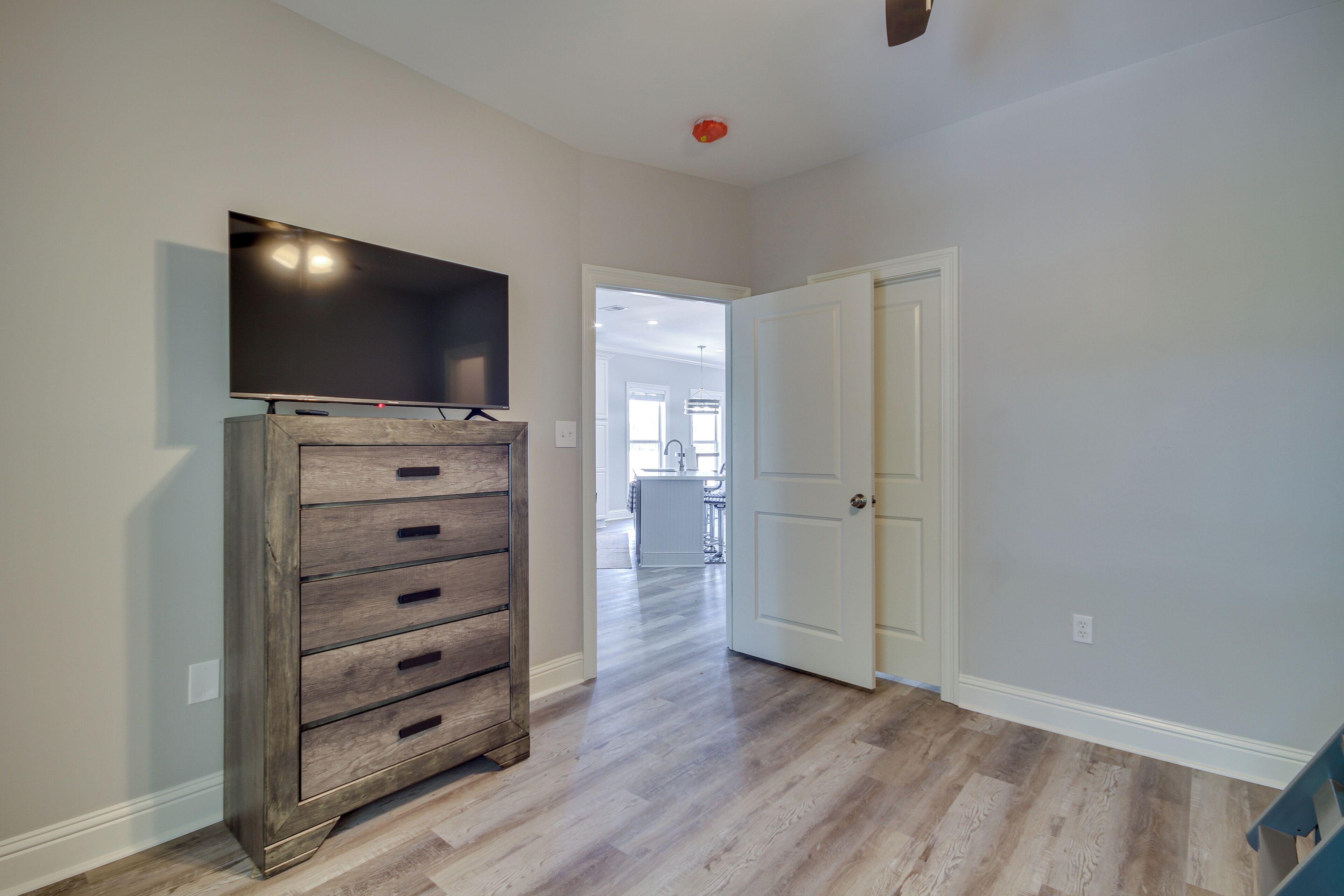 A hallway with a wooden cabinet and a flat-screen TV on the wall, leading to a door and a kitchen area in the background.