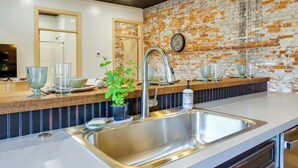 A modern kitchen with a stainless steel sink, a wooden countertop, and a brick wall. - Downtown Millersburg Retreat w/ Sleek Interior! (Millersburg)