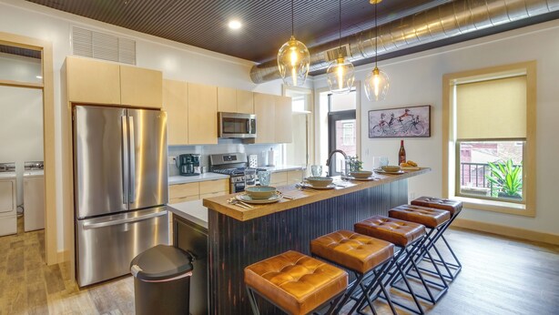 A modern kitchen with stainless steel appliances, a central island with bar stools, and pendant lighting. - Downtown Millersburg Retreat w/ Sleek Interior! (Millersburg)