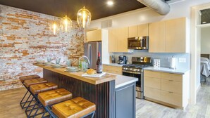 A modern kitchen with a brick wall, wooden bar stools, stainless steel appliances, and pendant lighting. - Downtown Millersburg Retreat w/ Sleek Interior! (Millersburg)