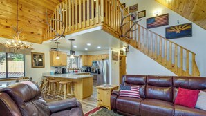A spacious living area with a brown leather sofa, a wooden staircase, and a kitchen in the background. - 2 Mi to Show Low Lake: Scenic Cabin w/ Balcony (Show Low)