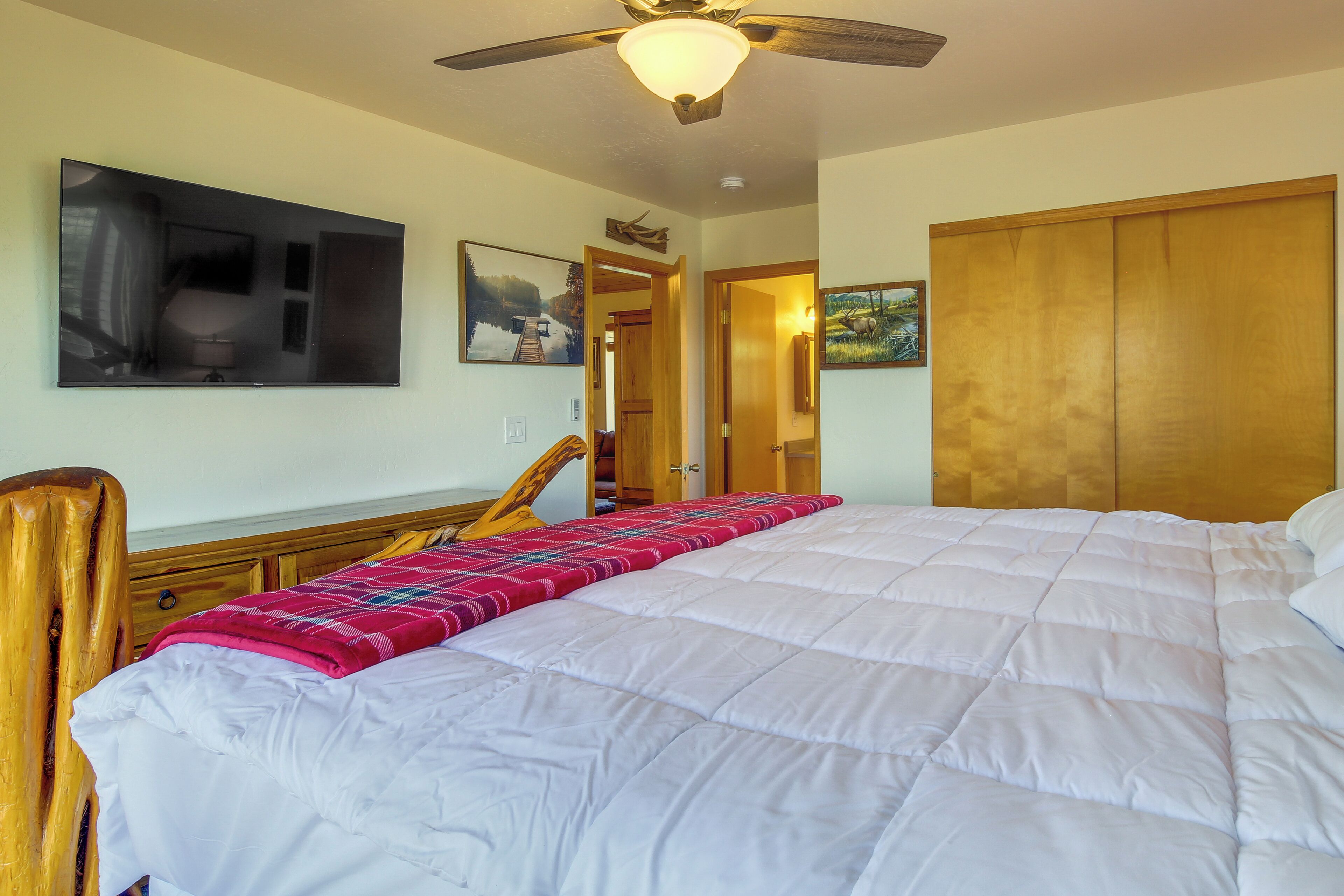 A bedroom with a large bed, wooden headboard, a ceiling fan, and a TV mounted on the wall.