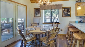 A rustic interior with a wooden dining table surrounded by mismatched chairs, a kitchen area with a bar stool, and a chandelier. - 2 Mi to Show Low Lake: Scenic Cabin w/ Balcony (Show Low)