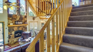 A wooden staircase with a stone fireplace and leather seating in a well-lit room. - 2 Mi to Show Low Lake: Scenic Cabin w/ Balcony (Show Low)