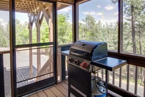 Een balkon met een barbecue en uitzicht op bomen.