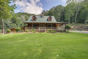 Une cabane en rondins avec un toit en métal vert, une véranda et une pelouse bien entretenue.
