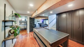 Une table de billard dans une pièce au plancher en bois, avec un escalier et un meuble de couleur sombre.