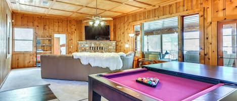 A wooden interior with a pool table, a sofa, and a fireplace.
